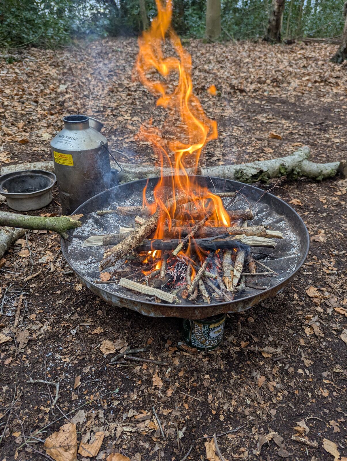 A campfire burning in a fire bowl with a kettle beside it