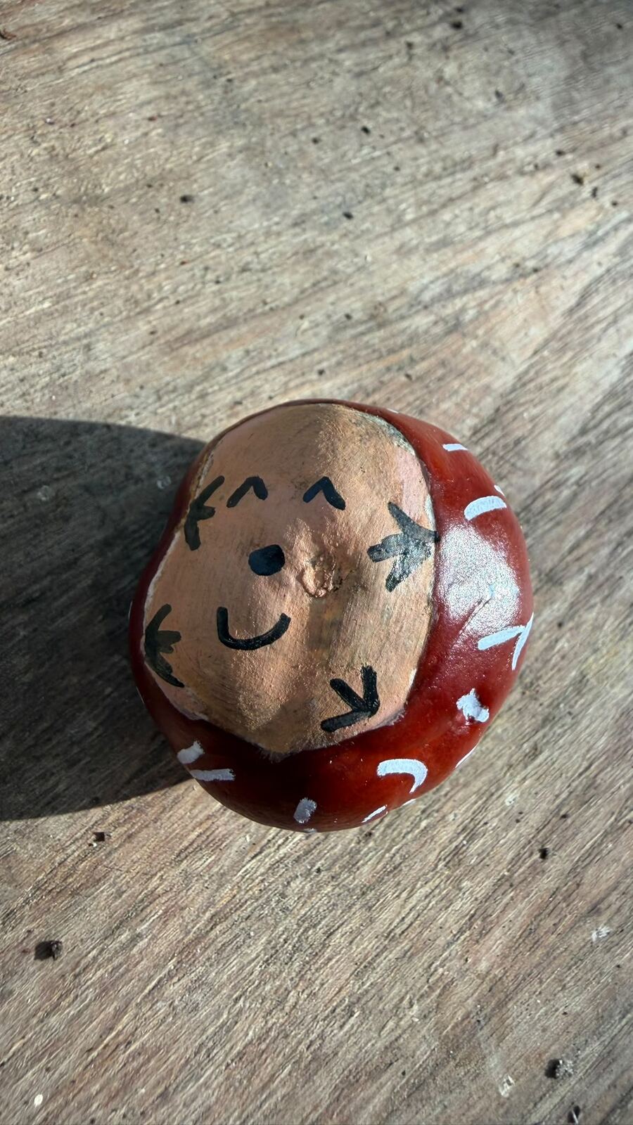 A conker painted with a smiling hedgehog face